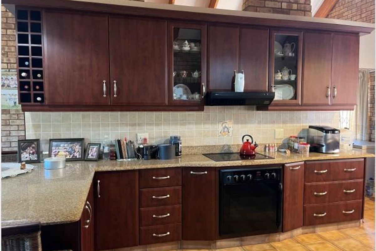 A traditional kitchen featuring dark wood cabinetry, granite countertops, a built-in oven, and a glass-top hob with an extractor fan.
