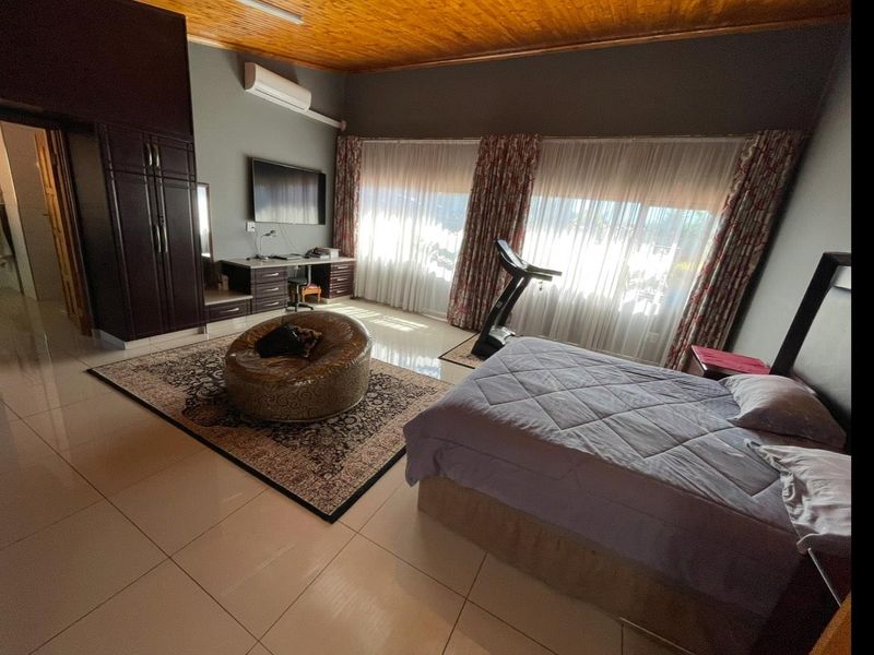 Spacious bedroom featuring tiled flooring, a timber ceiling, built-in cupboards, and a wall-mounted air conditioning unit.