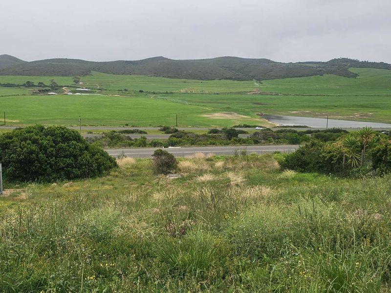 Expansive elevated view overlooking green fields, a small dam, and surrounding hills from the vacant residential plot.