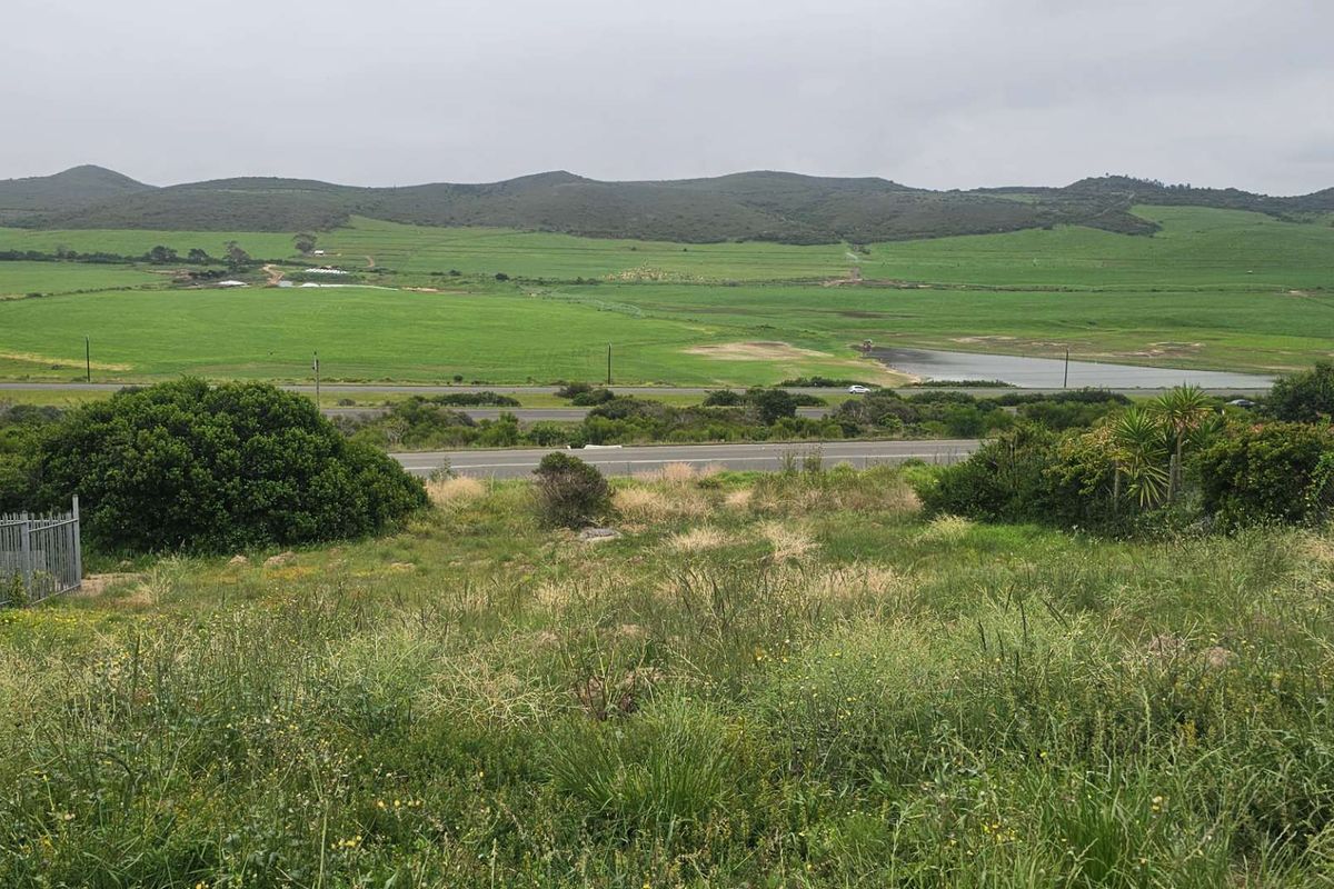 Expansive elevated view overlooking green fields, a small dam, and surrounding hills from the vacant residential plot.