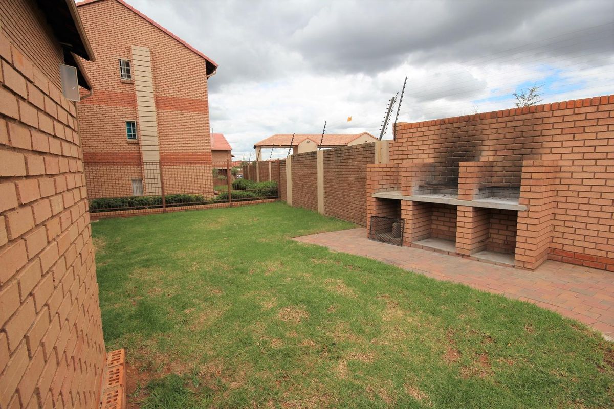 Private rear garden featuring a built-in brick braai, paved patio area, and established lawn, enclosed by a brick boundary wall with electric fencing.