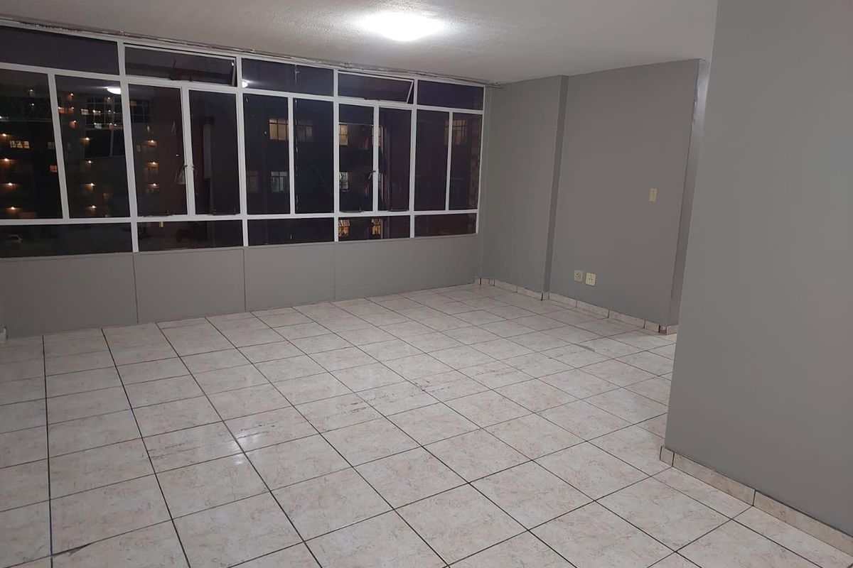 An empty living area featuring large windows, tiled flooring, and neutral grey walls, providing a versatile space for customization.