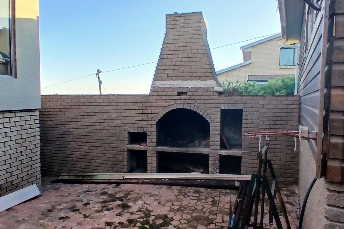 Rear patio area featuring a large built-in brick braai and chimney, set within a paved outdoor space.
