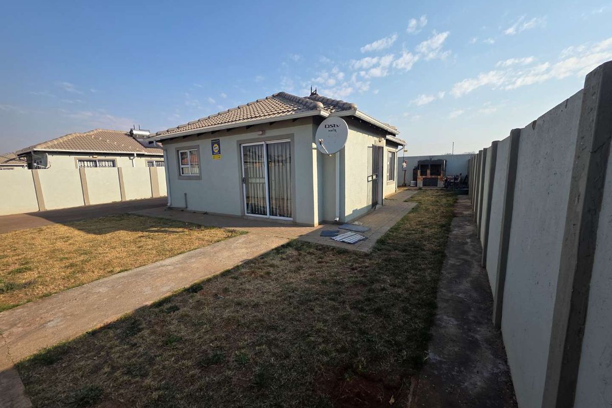 Rear view of the property featuring a tiled roof, sliding glass door, paved walkway, and a built-in braai area enclosed by a precast boundary wall.