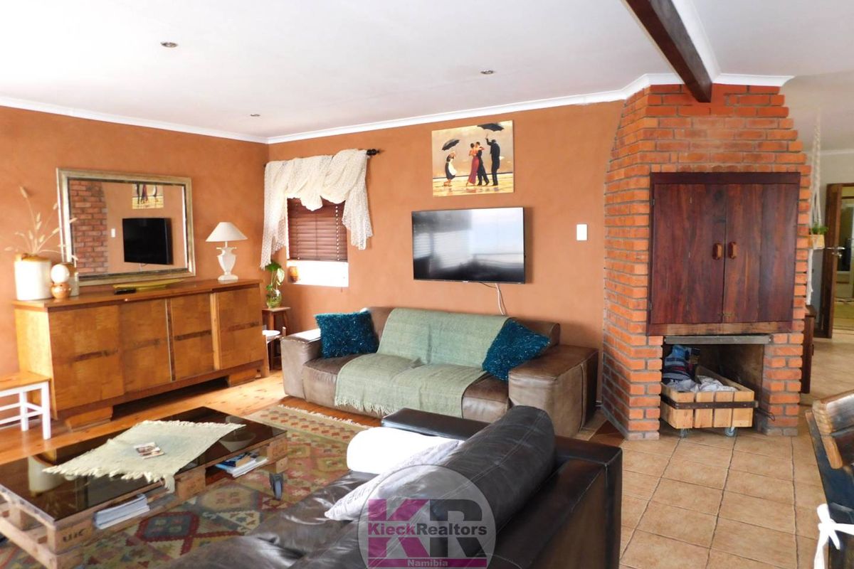 A cozy living room featuring a prominent exposed brick fireplace, tiled flooring, and recessed ceiling lighting.