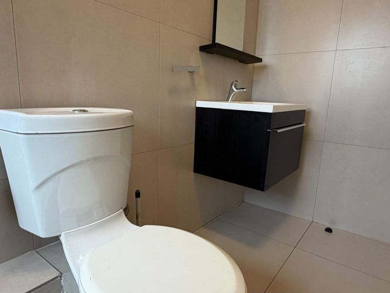 A modern, minimalist bathroom featuring a wall-mounted vanity, ceramic basin, and neutral wall and floor tiling.