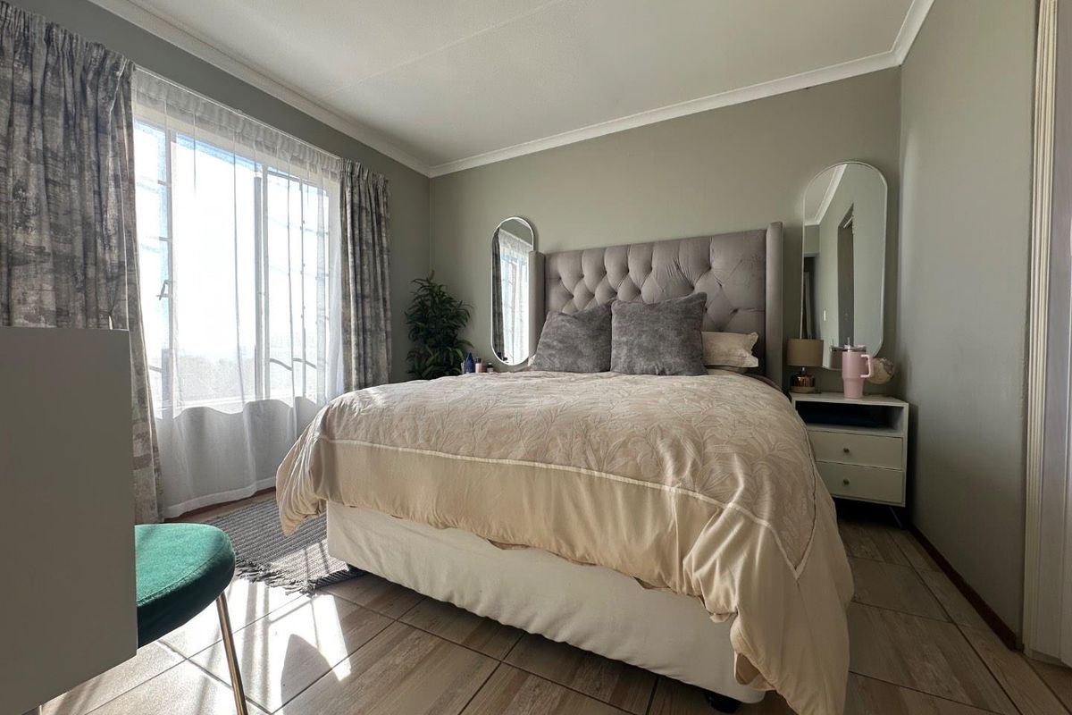 A well-maintained bedroom featuring tiled flooring, neutral wall tones, and a large window allowing for ample natural light.