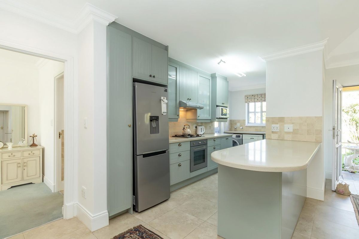 A well-maintained kitchen featuring sage green cabinetry, stone countertops, a breakfast bar, built-in oven, extractor fan, and tiled flooring.
