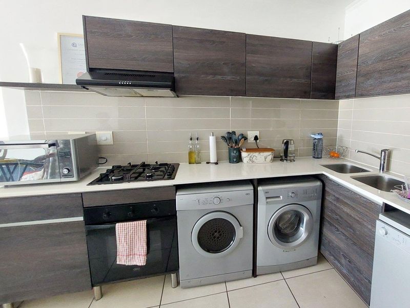 A functional kitchen featuring dark wood-grain cabinetry, a gas hob, built-in oven, extractor fan, and integrated laundry appliances with a tiled backsplash.