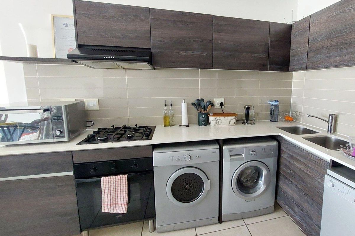 A functional kitchen featuring dark wood-grain cabinetry, a gas hob, built-in oven, extractor fan, and integrated laundry appliances with a tiled backsplash.