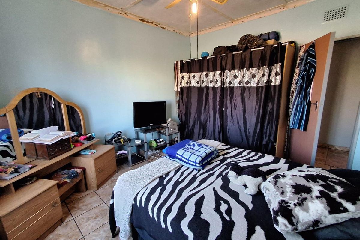 A bedroom featuring tiled flooring, a ceiling fan, and a built-in wardrobe, currently showing signs of wear on the ceiling finishes.