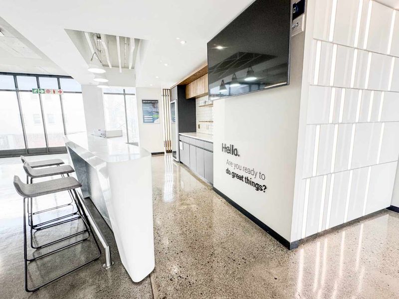 Modern office kitchen area featuring polished concrete floors, sleek built-in cabinetry, a stone breakfast bar, and contemporary wall finishes.