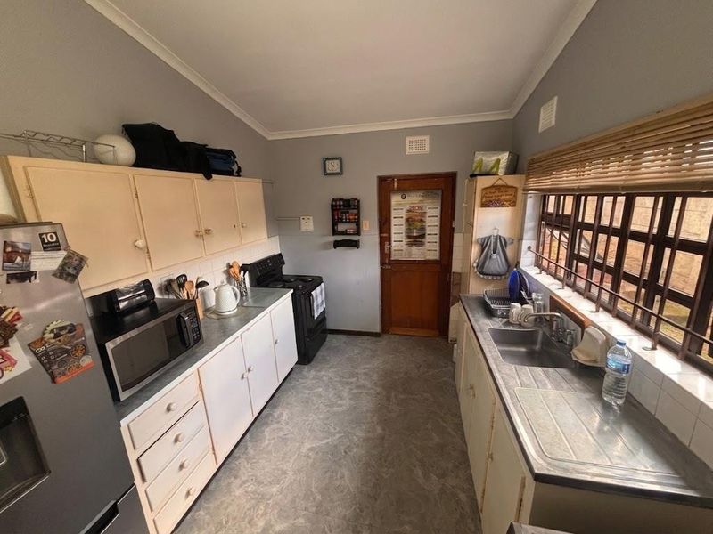 A functional kitchen featuring laminate cabinetry, a stainless steel sink, and a freestanding stove, with potential for cosmetic updates to modernize the space.