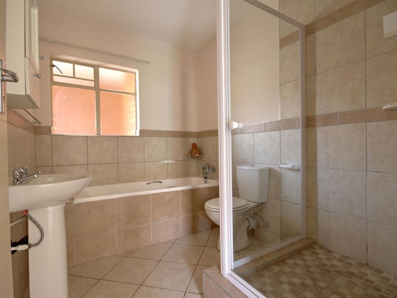 A functional bathroom featuring a pedestal basin, built-in bathtub, and a separate shower enclosure with tiled finishes throughout.