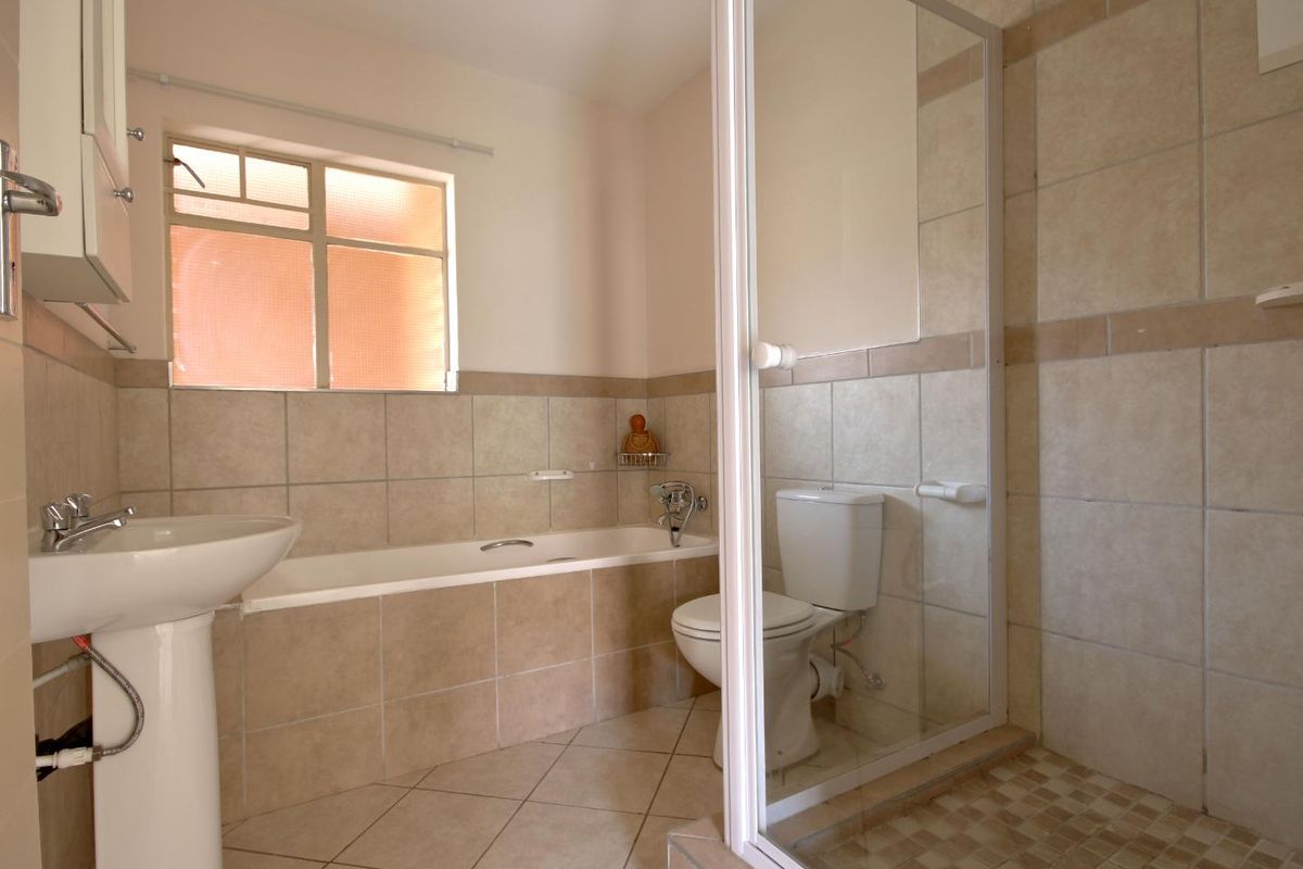 A functional bathroom featuring a pedestal basin, built-in bathtub, and a separate shower enclosure with tiled finishes throughout.