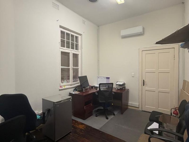 A functional office space featuring timber flooring, air conditioning, and recessed ceiling speakers, suitable for a home workspace or study.