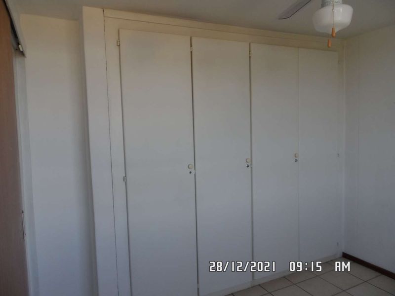 A simple bedroom featuring built-in cupboards, a ceiling fan, and tiled flooring.