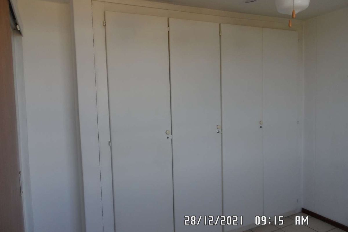A simple bedroom featuring built-in cupboards, a ceiling fan, and tiled flooring.