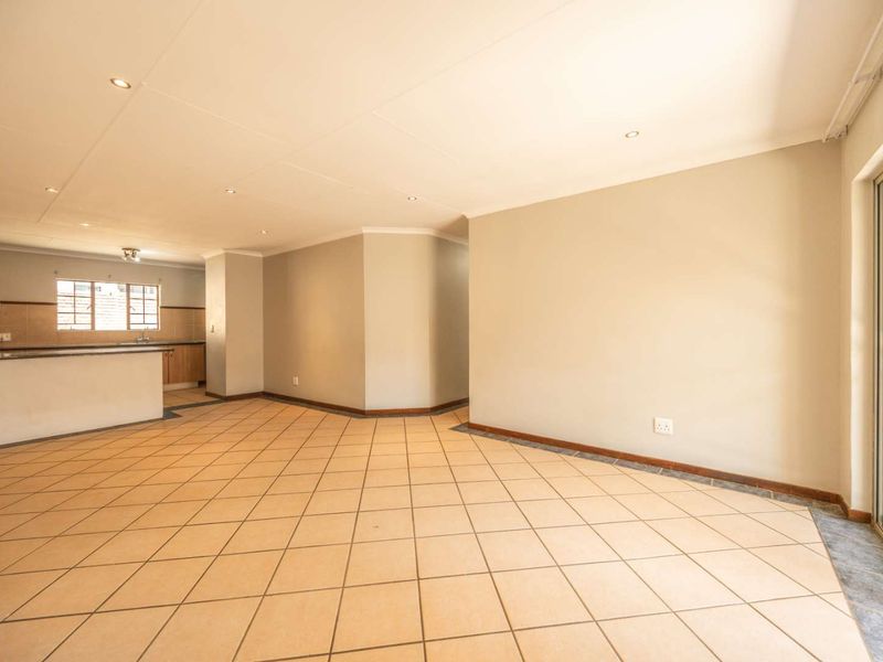 Spacious open-plan living area featuring tiled flooring, recessed lighting, and a sliding glass door leading to the exterior, with an adjacent kitchen space.
