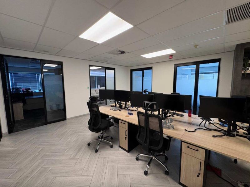 Modern open-plan office space featuring herringbone tile flooring, suspended ceilings with recessed lighting, and glass partition doors providing a professional work environment.