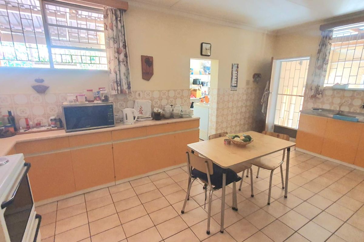 A spacious kitchen featuring dated cabinetry, tiled flooring, and a functional layout with an adjacent scullery area and direct outdoor access.
