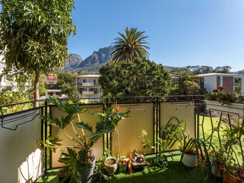 A balcony featuring metal railings and artificial grass flooring, offering scenic views of the surrounding neighborhood and mountain landscape.
