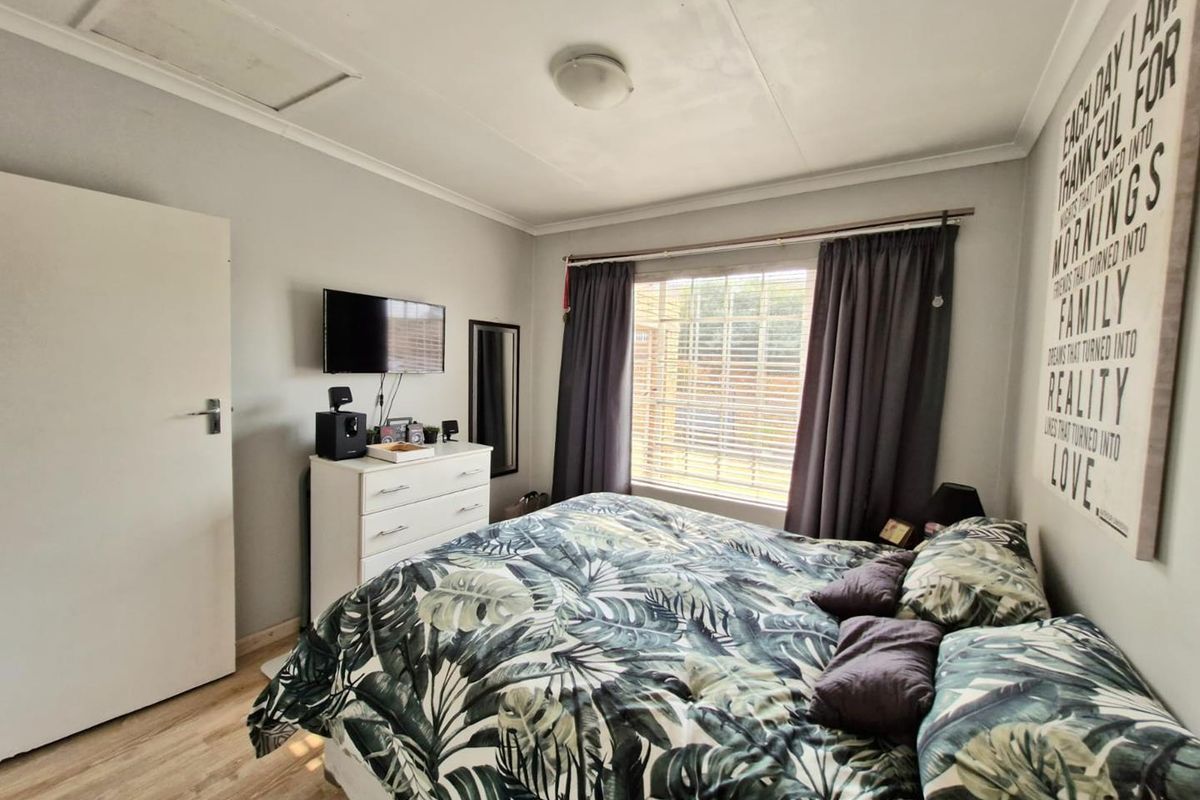 A well-lit bedroom featuring laminate flooring, a window with curtain tracks, and a ceiling-mounted light fixture.