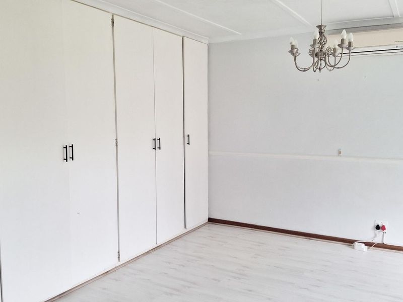A bright, empty bedroom featuring white built-in cupboards, light-toned laminate flooring, and a wall-mounted air conditioning unit.