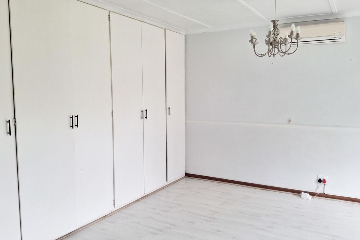 A bright, empty bedroom featuring white built-in cupboards, light-toned laminate flooring, and a wall-mounted air conditioning unit.