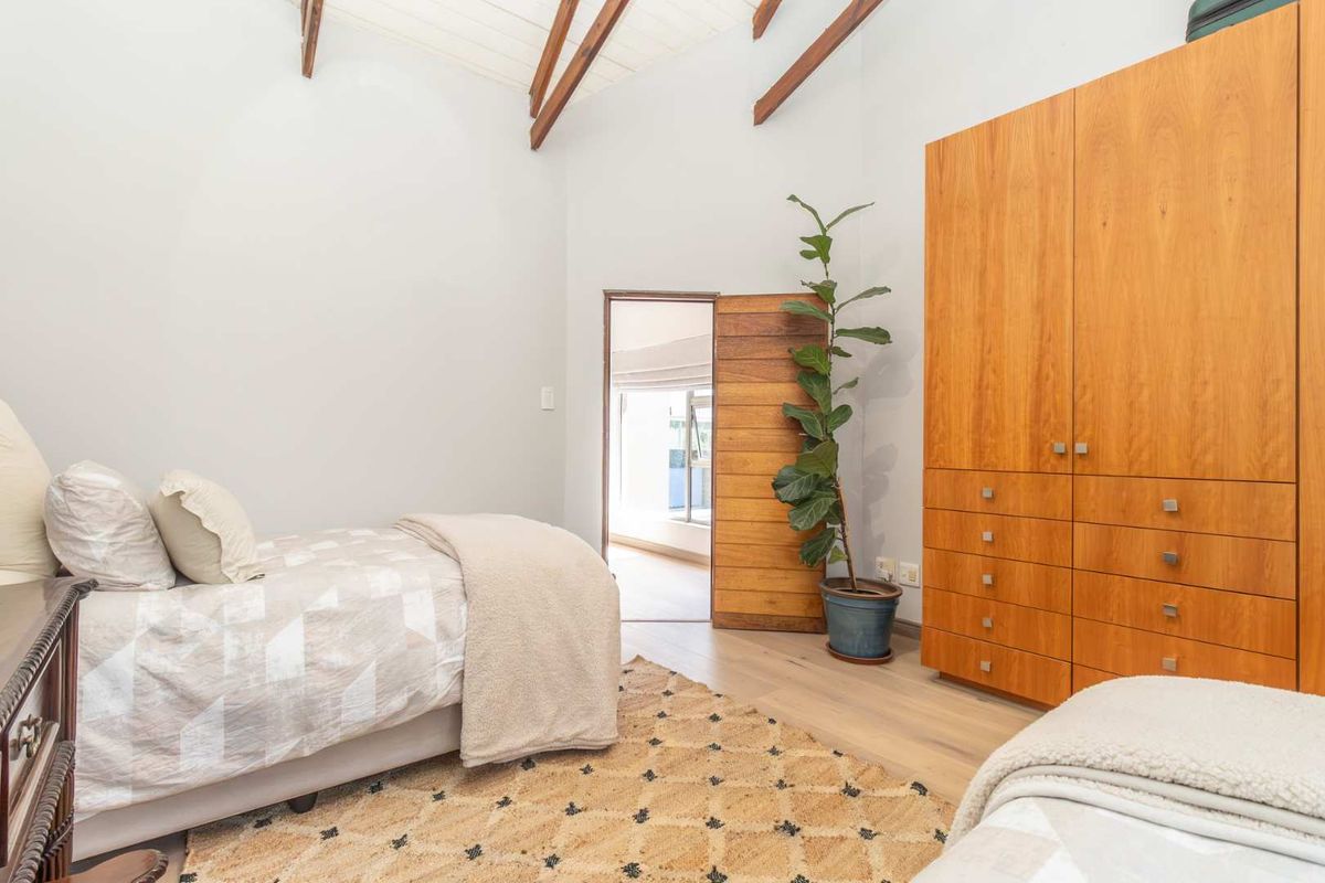 A bright bedroom featuring high vaulted ceilings with exposed timber beams, light wood-look flooring, and built-in floor-to-ceiling wooden cabinetry.