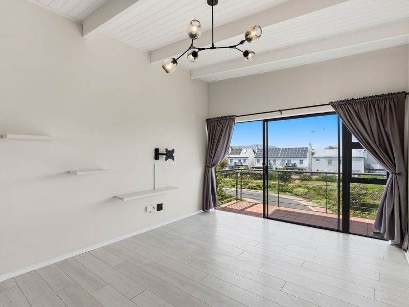 Bright living area featuring vaulted ceilings with exposed beams, modern laminate flooring, and sliding glass doors opening onto a private balcony.