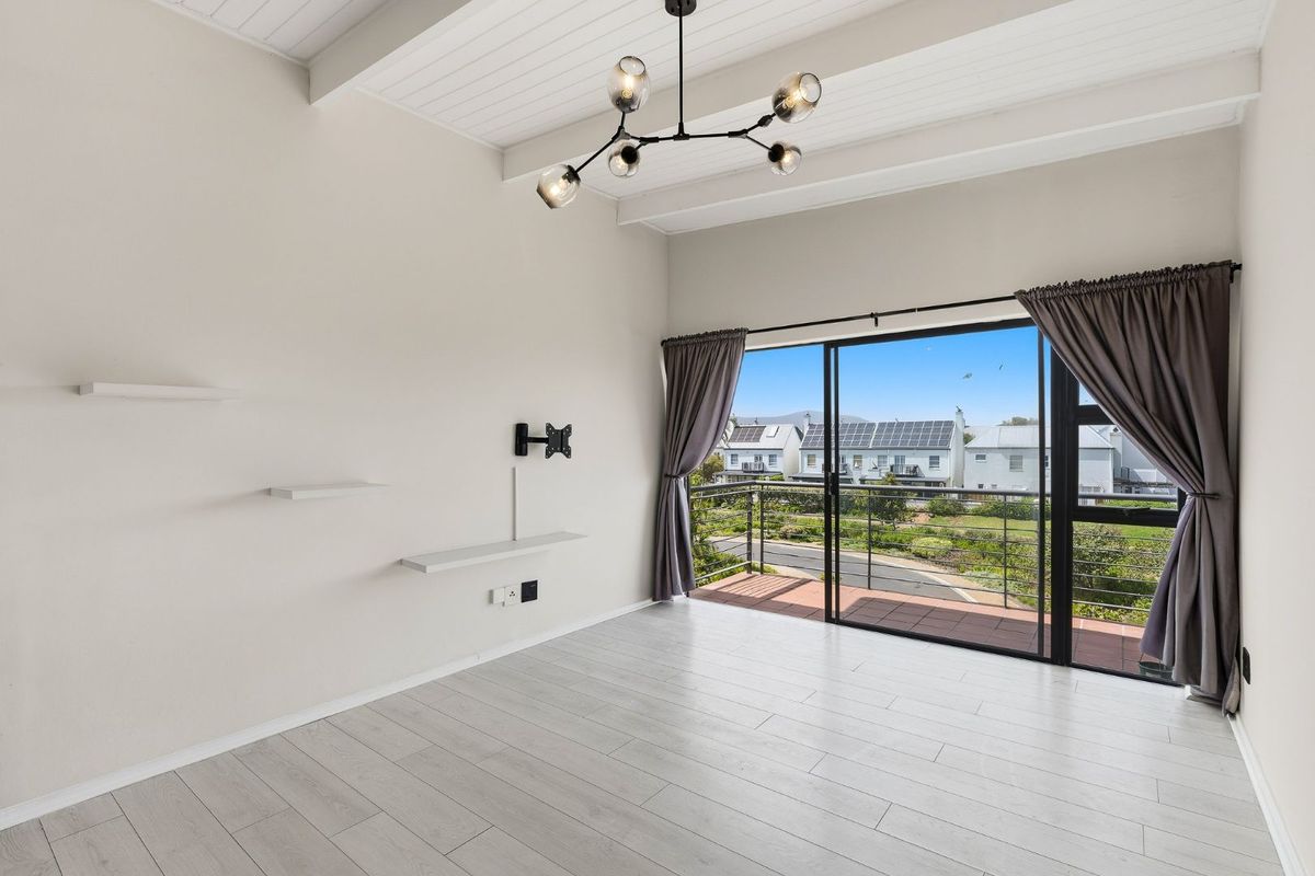 Bright living area featuring vaulted ceilings with exposed beams, modern laminate flooring, and sliding glass doors opening onto a private balcony.
