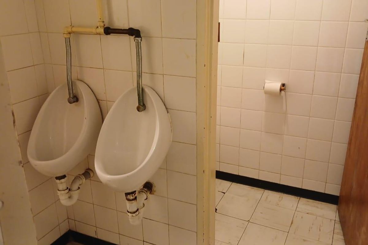 A commercial restroom facility featuring wall-mounted urinals and tiled surfaces, showing signs of age and wear.