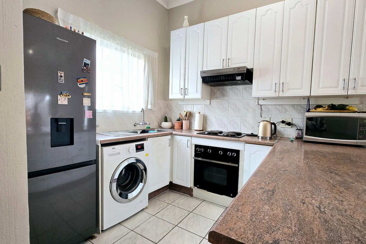 Compact kitchen featuring white cabinetry, built-in oven with hob, extractor fan, integrated sink, and space for a washing machine.