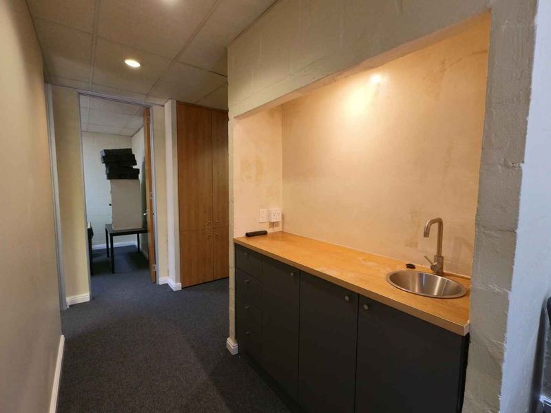 A functional office utility area featuring built-in cabinetry, a stainless steel sink, and recessed lighting, providing convenient kitchenette facilities within the workspace.