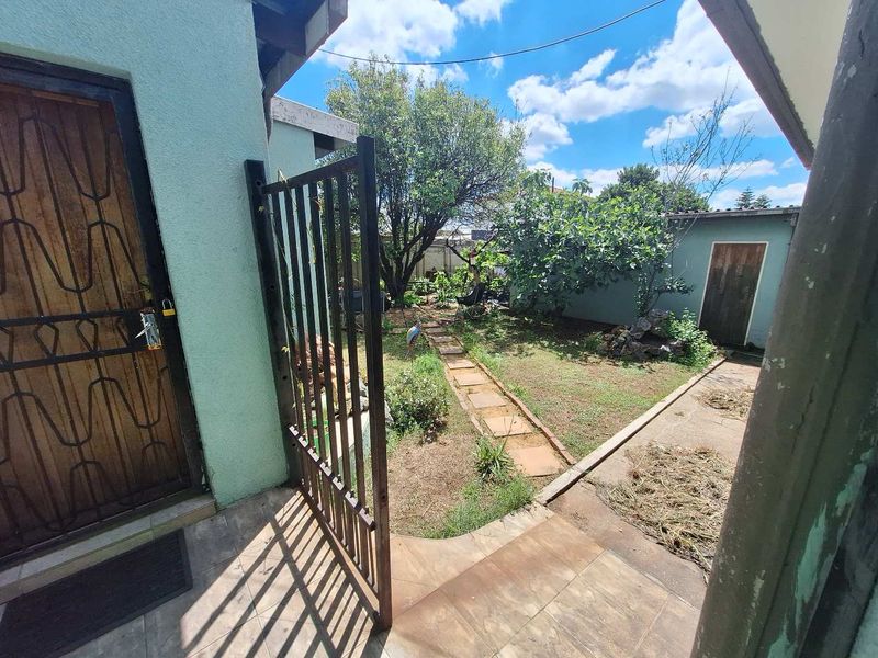 A rear garden area featuring a paved walkway, security gate, and access to the main dwelling and a secondary structure.