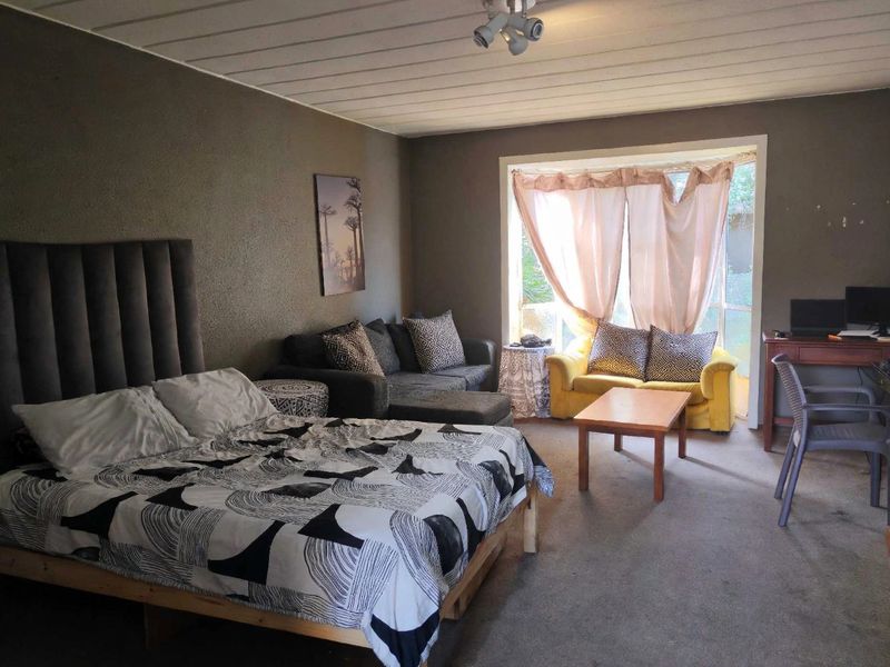 Spacious bedroom featuring a large window for natural light and a distinctive tongue and groove ceiling, offering a versatile layout for living and sleeping.