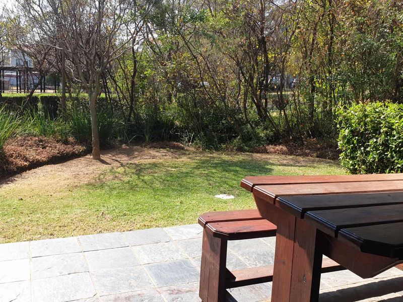 A private stone-paved patio area overlooking a lush, established garden with mature trees and greenery.