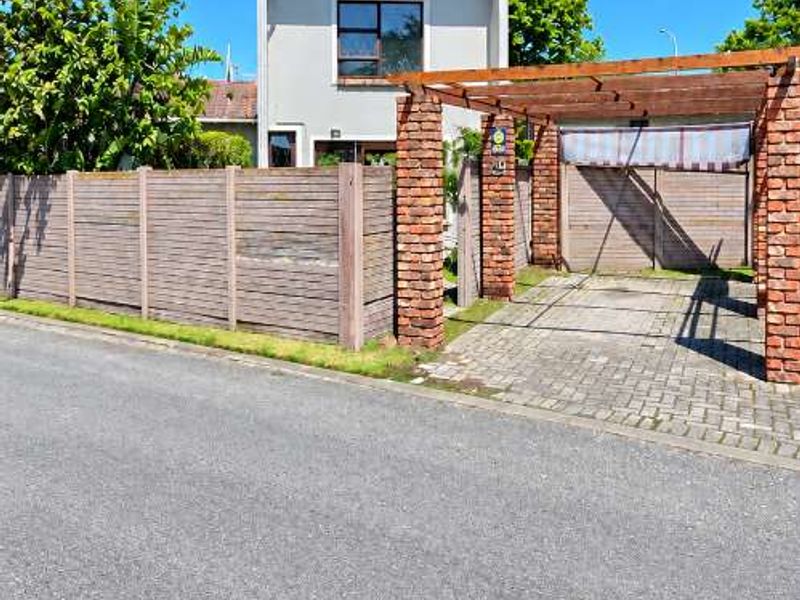 Front exterior view of the townhouse featuring a paved driveway, brick pillars with a timber pergola, and a timber boundary fence.