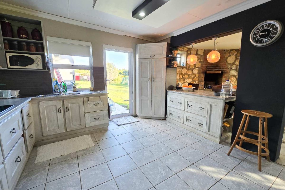 Rustic farmhouse kitchen featuring light-toned cabinetry, tiled flooring, and a stone-accented indoor braai area with direct access to the garden.