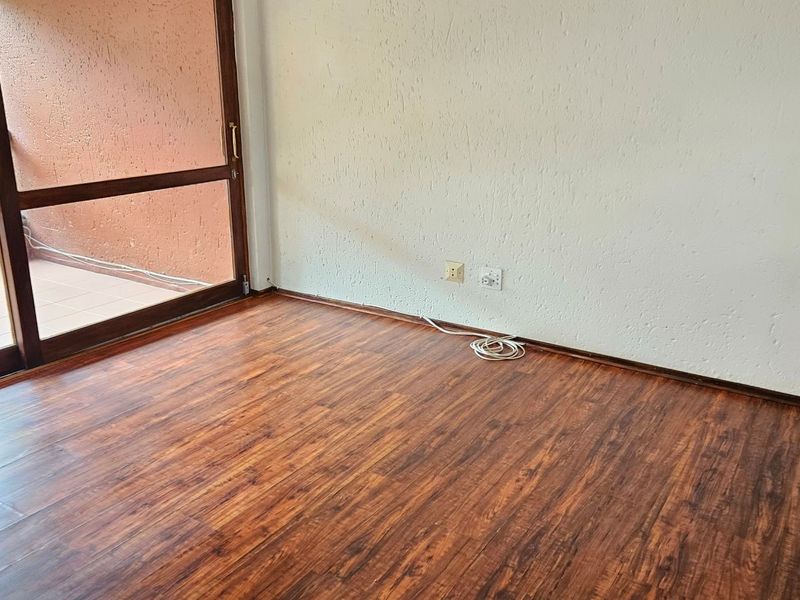 An empty living room featuring dark wood-look laminate flooring, textured walls, and a large sliding glass door providing access to an outdoor balcony.