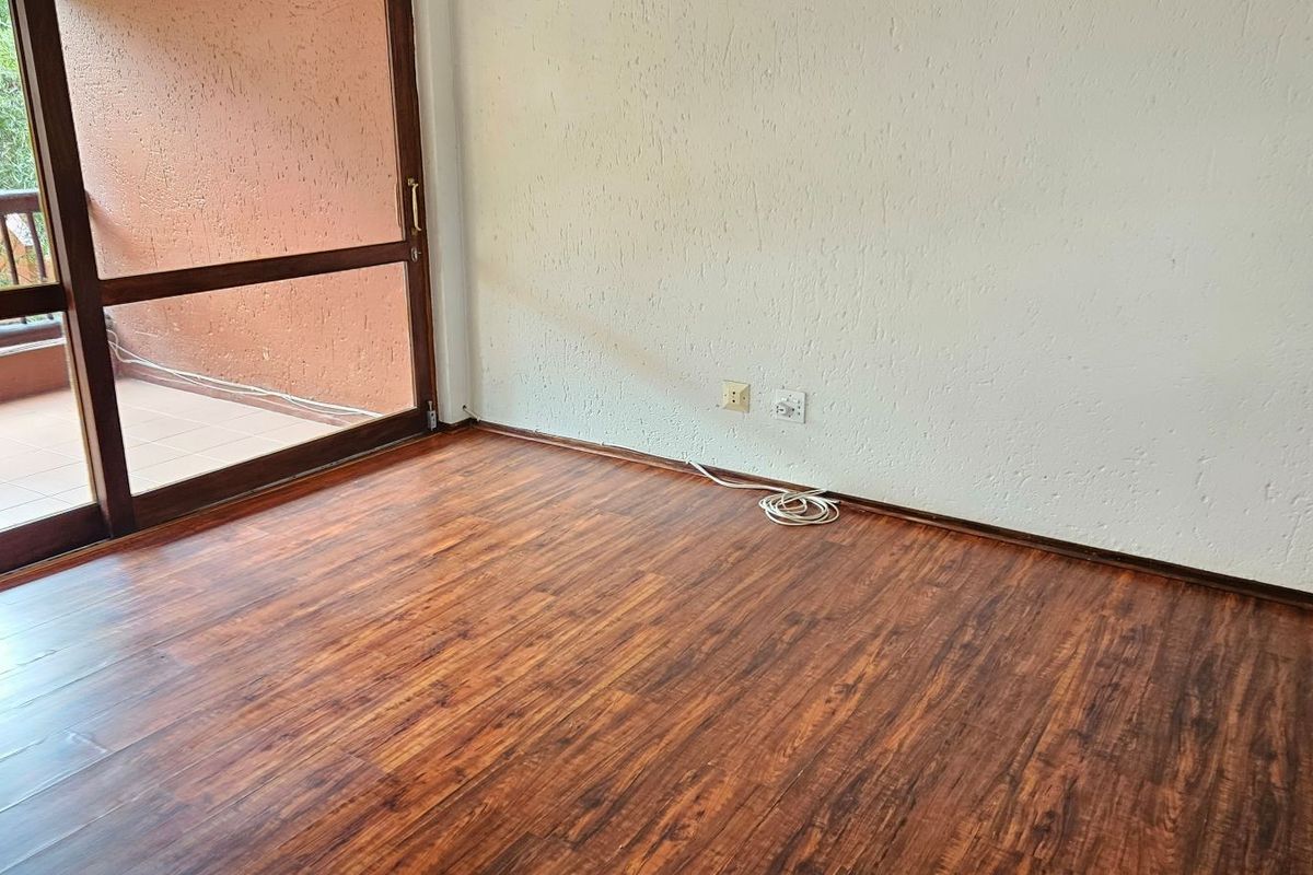 An empty living room featuring dark wood-look laminate flooring, textured walls, and a large sliding glass door providing access to an outdoor balcony.