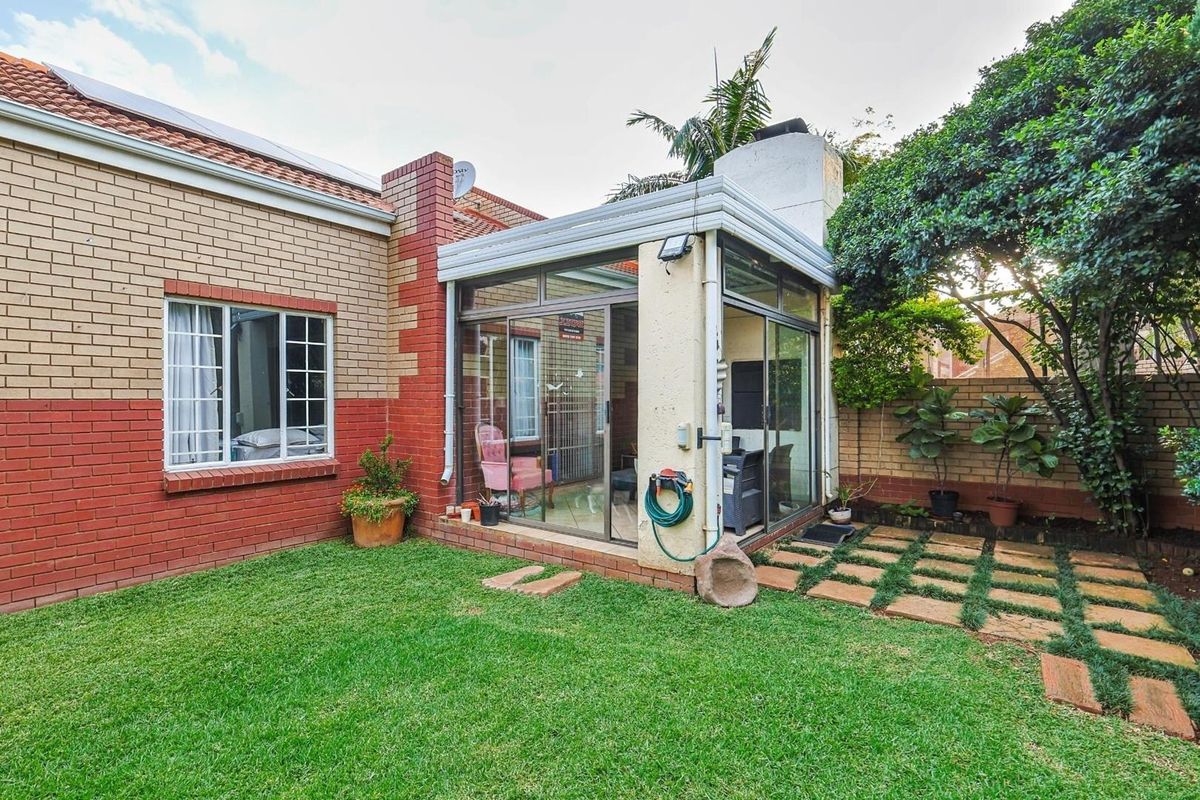 A rear view of the townhouse featuring a brick facade, a glass-enclosed patio area, and a well-maintained garden with paved stepping stones.