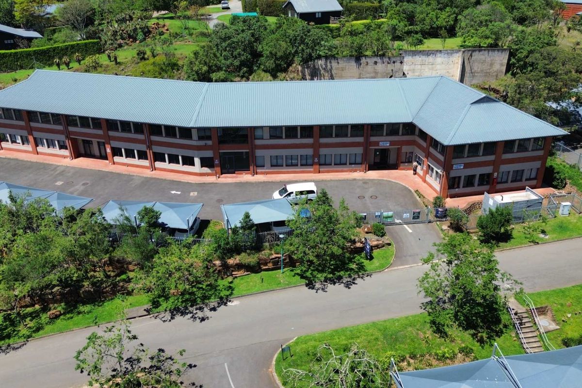 Aerial view of a two-story office building featuring a metal roof, brick facade, and an adjacent asphalt parking area with shade cloth carports.