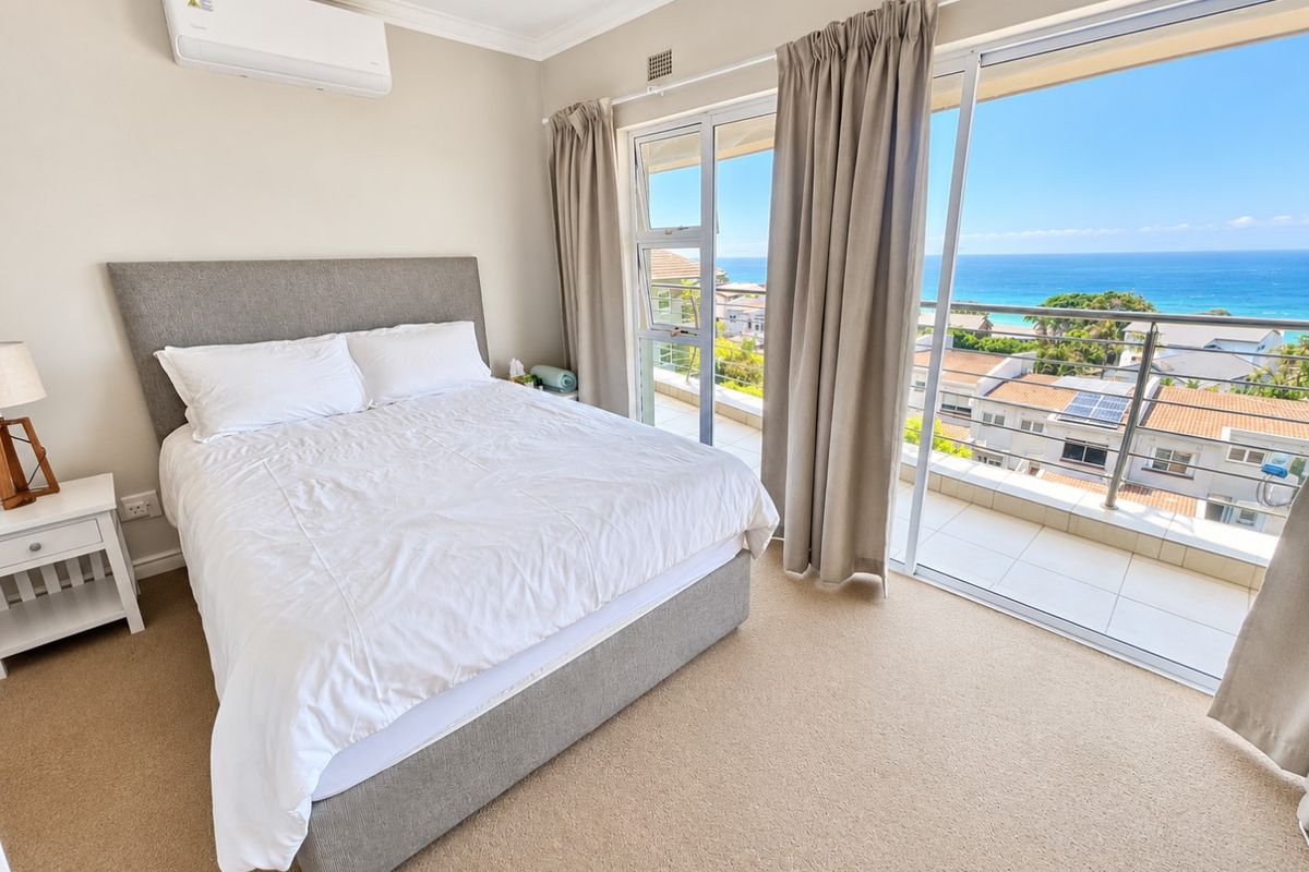 A well-maintained bedroom featuring carpeted flooring, a wall-mounted air conditioner, and large sliding glass doors opening onto a balcony with ocean views.