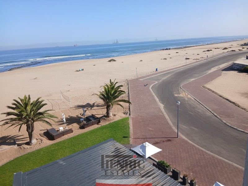 Elevated coastal view overlooking the beach, paved promenade, and ocean horizon.