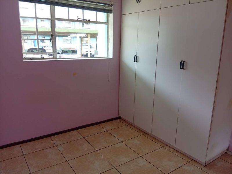 An empty bedroom featuring built-in cupboards, tiled flooring, and a window with security bars, offering a blank canvas for renovation.