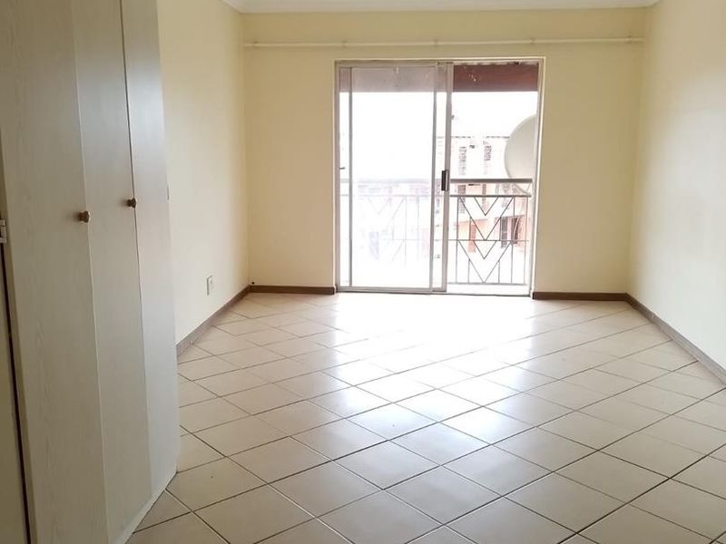 An empty living room featuring tiled flooring, built-in cupboards, and a sliding glass door leading to a balcony.