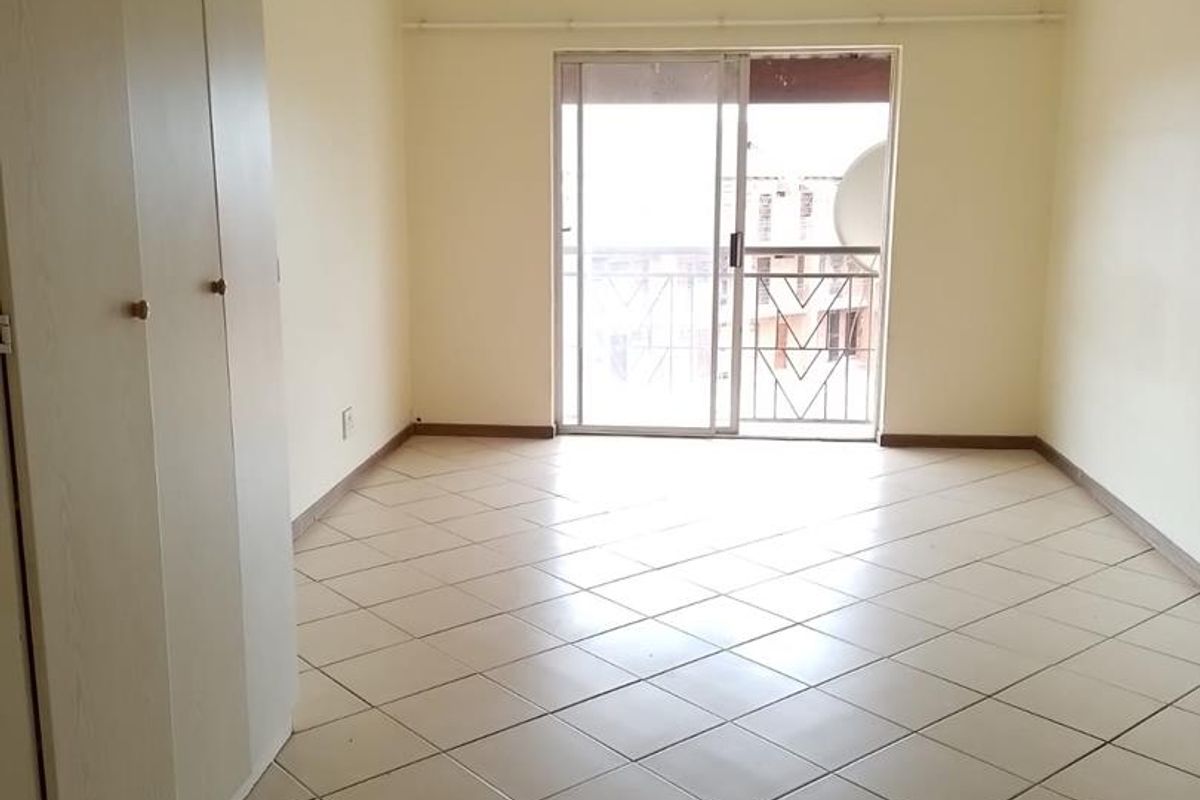 An empty living room featuring tiled flooring, built-in cupboards, and a sliding glass door leading to a balcony.