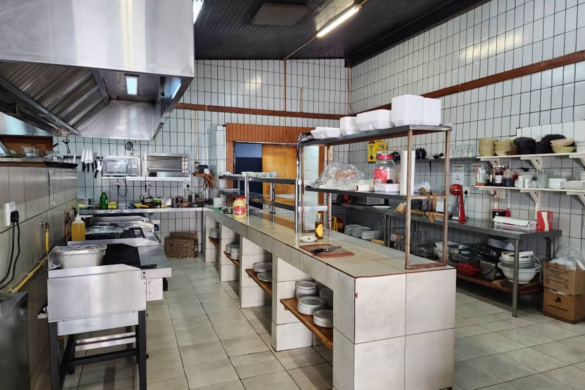 Commercial kitchen featuring tiled walls and flooring, stainless steel extractor hood, and built-in tiled service counters for efficient food preparation and service.